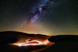 A clear night sky of stars over sand dunes